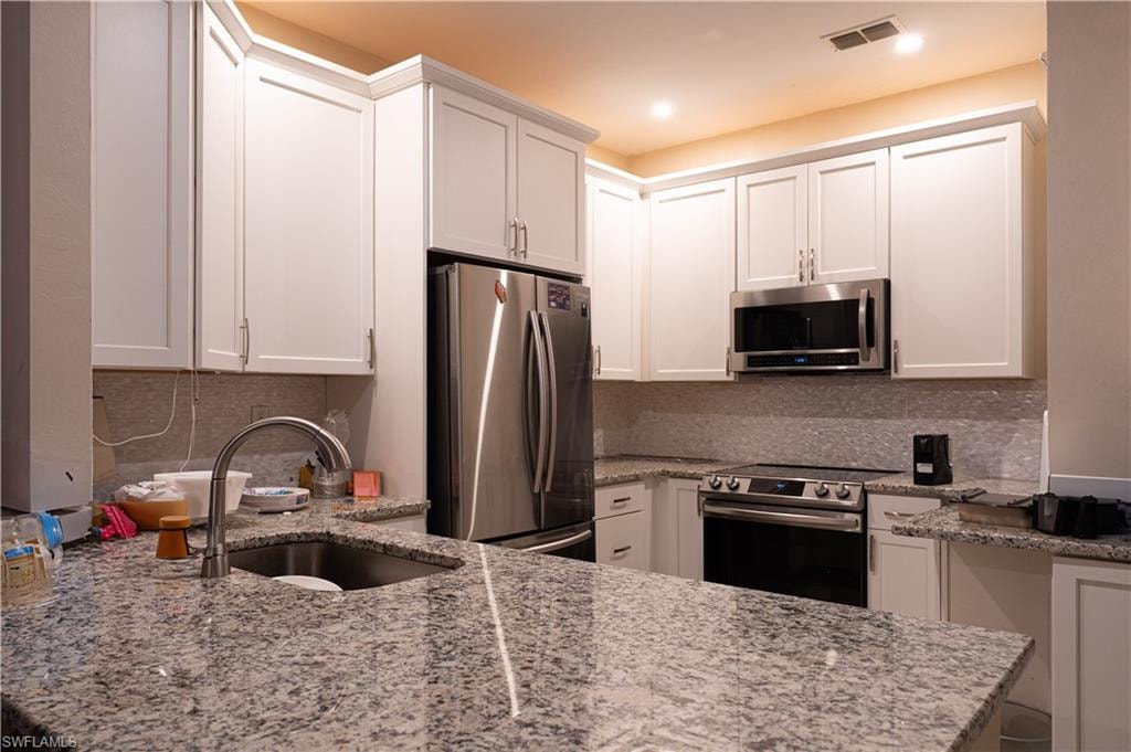 Kitchen with appliances with stainless steel finishes, white cabinets, light stone countertops, sink, and kitchen peninsula