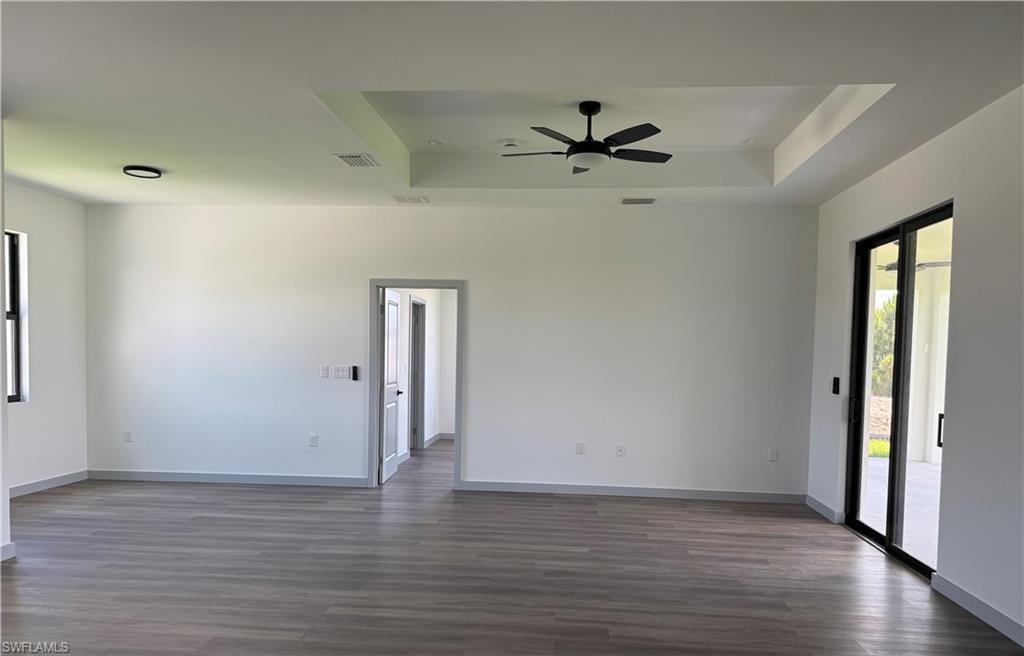 Spacious interior featuring wood-finish flooring, a tray ceiling with a ceiling fan, and white walls