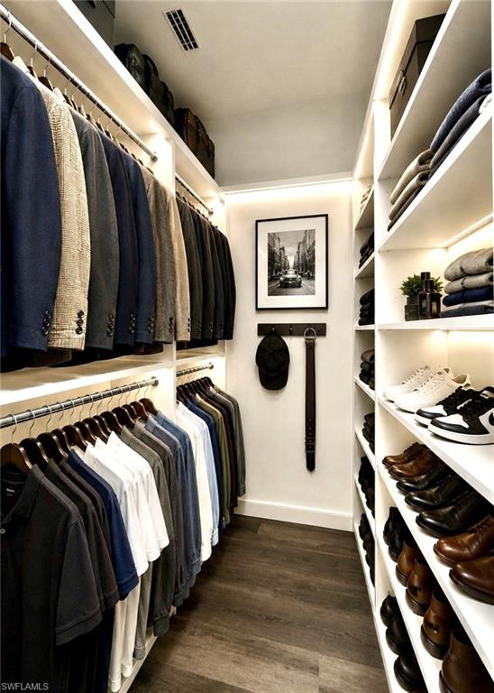 Gentleman's Walk-in closet featuring extensive built-in shelving and hanging rods, integrated lighting, wood-finish flooring, and a ceiling ventilation system-Virtually Staged