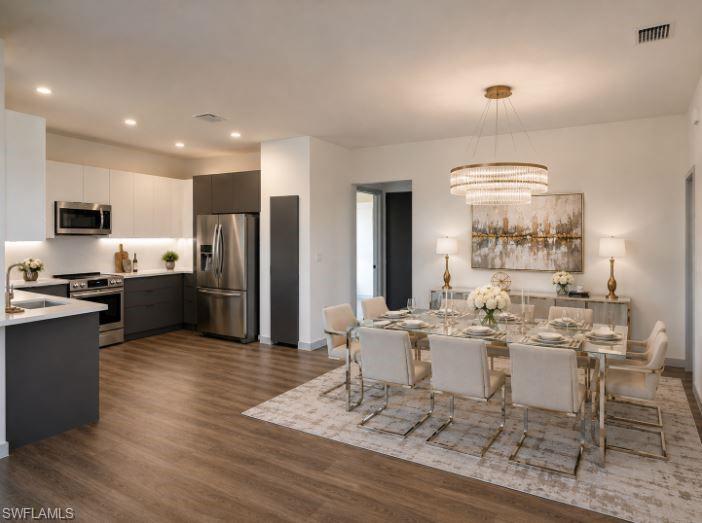 Open-concept kitchen and dining area featuring wood-finish flooring, two-tone cabinetry, stainless steel appliances, and a tiered crystal chandelier