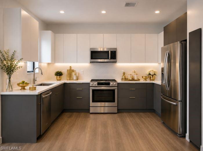 Modern kitchen featuring two-tone cabinetry, stainless steel appliances, under-cabinet lighting, wood-finish flooring, and recessed ceiling lighting