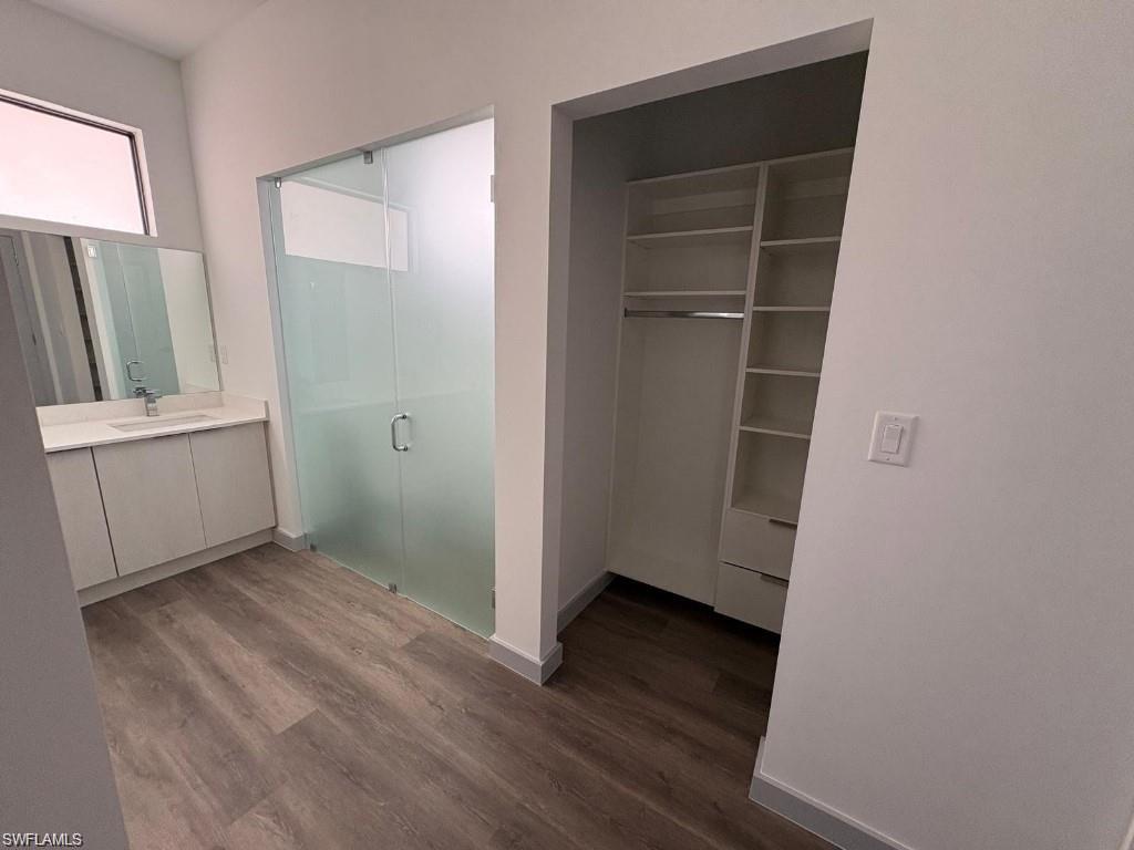 Contemporary bathroom featuring a frosted glass shower enclosure, single vanity with a white countertop, and wood-finish flooring