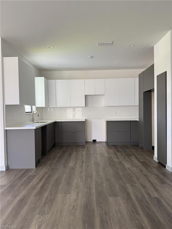 Modern kitchen featuring wood-finish flooring, two-tone cabinetry with white upper and gray lower cabinets, light-toned countertops, and a full-height backsplash