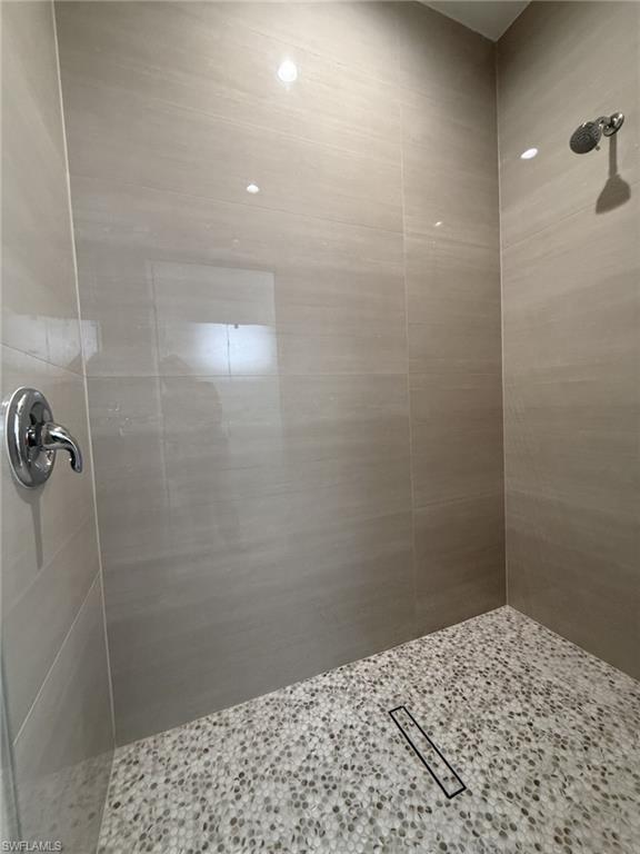 Walk-in shower featuring large format wall tiles, pebble-style floor tiling, a linear drain, and chrome fixtures
