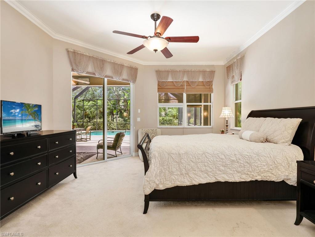 Primary Bedroom with Crown Molding, Window Coverings, Ceiling Fan, & Sliders Leading to the Screened-In Lanai with a Pool View