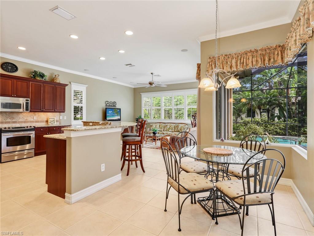 Kitchen with 42" Cabinetry, Stainless Steel Appliances & Breakfast Bar, Eat-In Kitchen with Large Frameless Window with Pool View, & Family Room with Plantation Shutters & Sliders Leading to the Screened-In Lanai