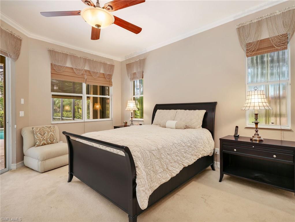 Primary Bedroom with Crown Molding, Window Coverings, Ceiling Fan, & Sliders Leading to the Screened-In Lanai with a Pool View