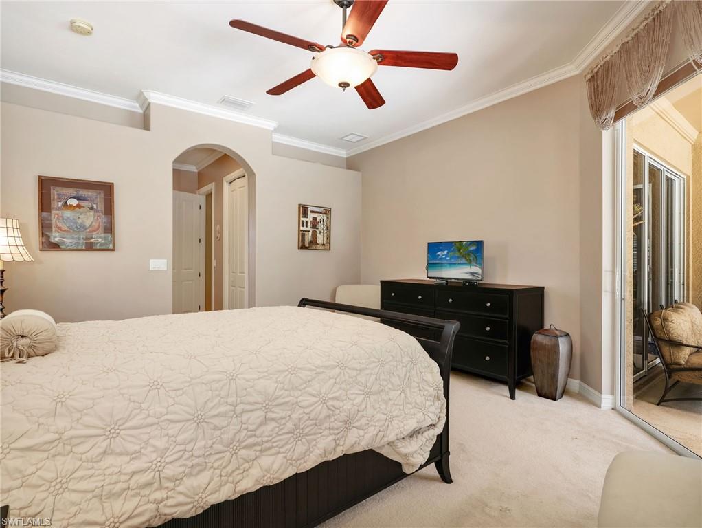 Primary Bedroom with Crown Molding, Window Coverings, Ceiling Fan, & Sliders Leading to the Screened-In Lanai with a Pool View & Entrance to the En-Suite Bathroom