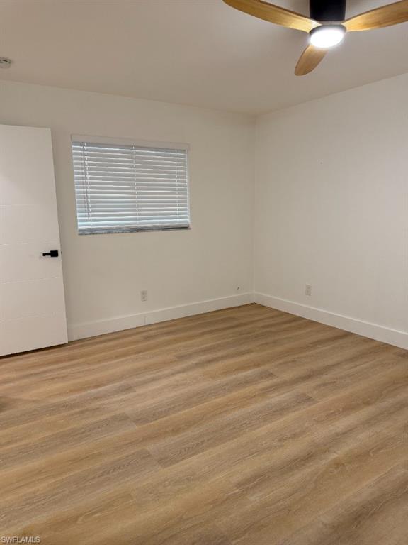 Spacious room featuring wood-finish flooring, crisp white walls, and a contemporary ceiling fan with integrated lighting