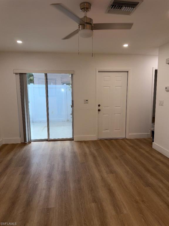 Spacious room featuring wood-finish flooring, white walls, and a ceiling fan with integrated lighting