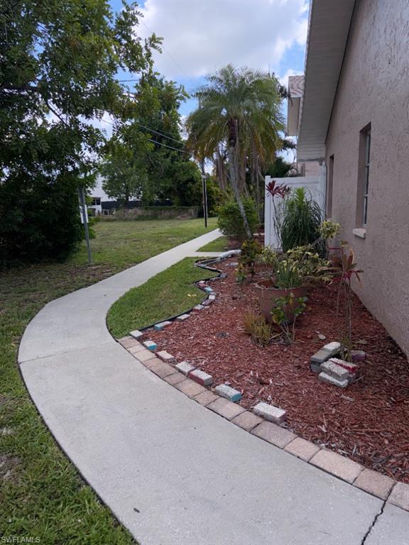 Curved concrete pathway bordering a mulched garden bed with various plantings