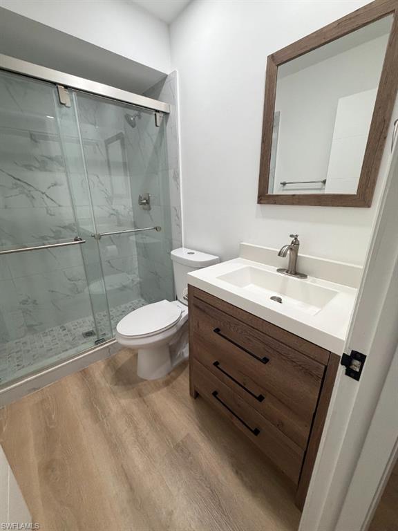 Bathroom featuring a wood-finish vanity with a white countertop and integrated sink, a glass-enclosed shower with marble-look wall tiles, and wood-look flooring