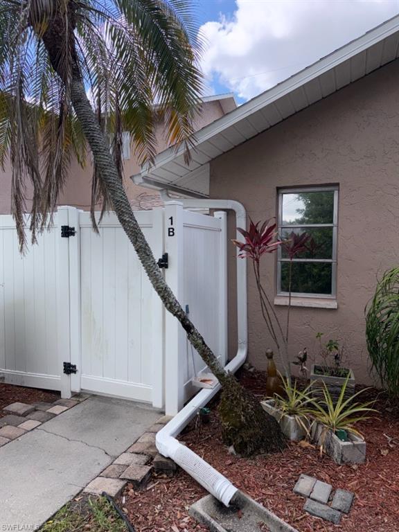 Exterior featuring a palm tree, white vinyl fencing, stucco siding, and a single window
