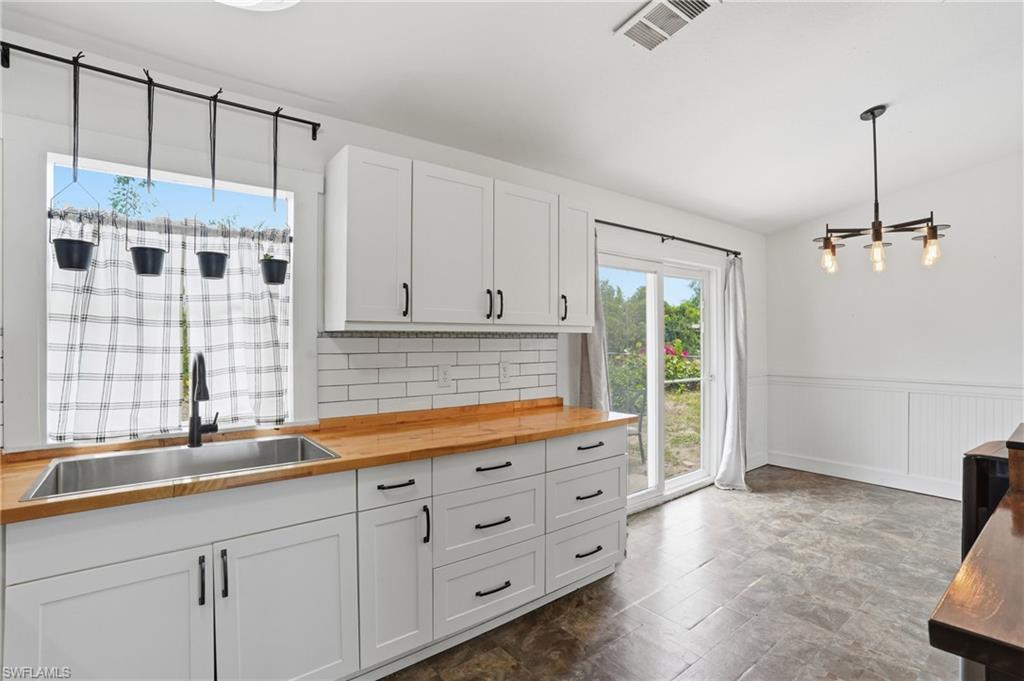 Kitchen featuring white shaker cabinetry, butcher block countertops, a stainless steel sink with a matte black faucet, and a subway tile backsplash
