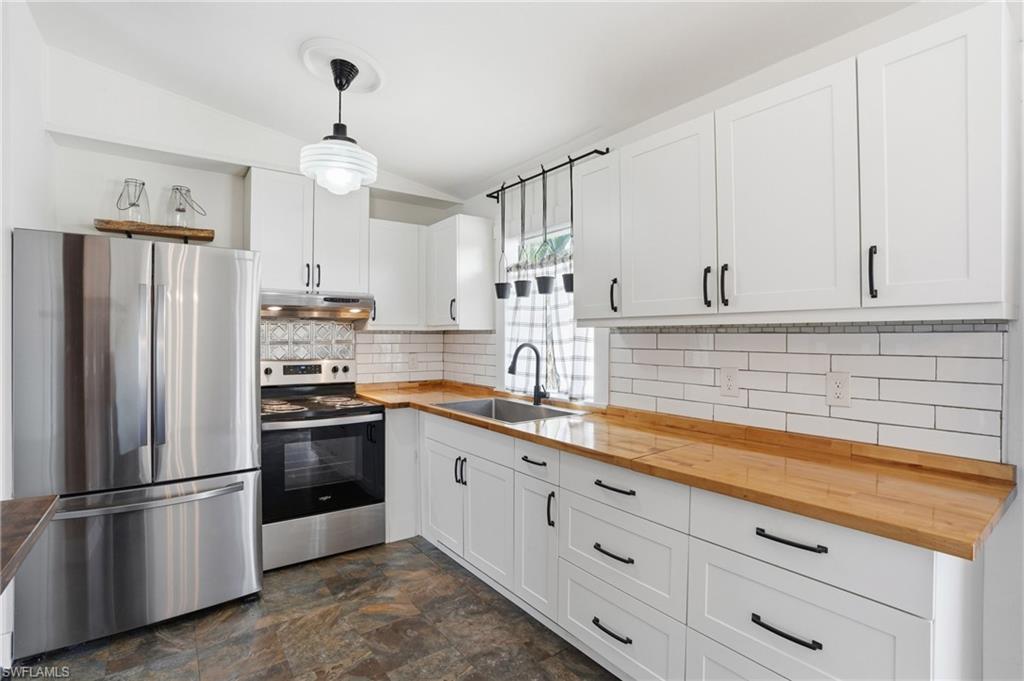 Kitchen featuring white shaker-style cabinetry, wood-finish countertops, stainless steel appliances, white subway tile backsplash, and slate-style flooring
