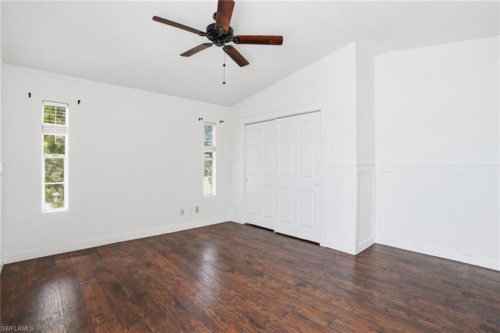 Room featuring wood-finish flooring, vaulted ceilings, a ceiling fan, and paneling accents