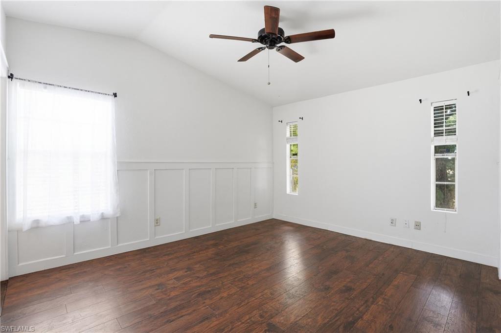Spacious room featuring wood-finish flooring, white board and batten wall detailing, and a vaulted ceiling with a ceiling fan