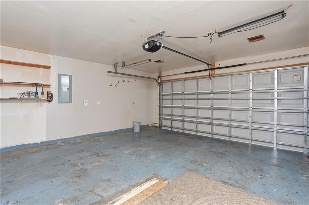 Spacious garage with an automatic overhead door, concrete flooring, overhead lighting, and built-in shelving