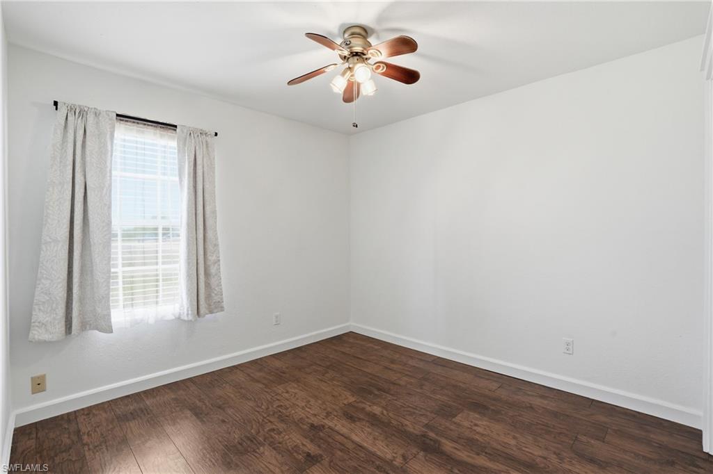Spacious room featuring wood-finish flooring, a ceiling fan with integrated lighting, white walls, and a large window with blinds