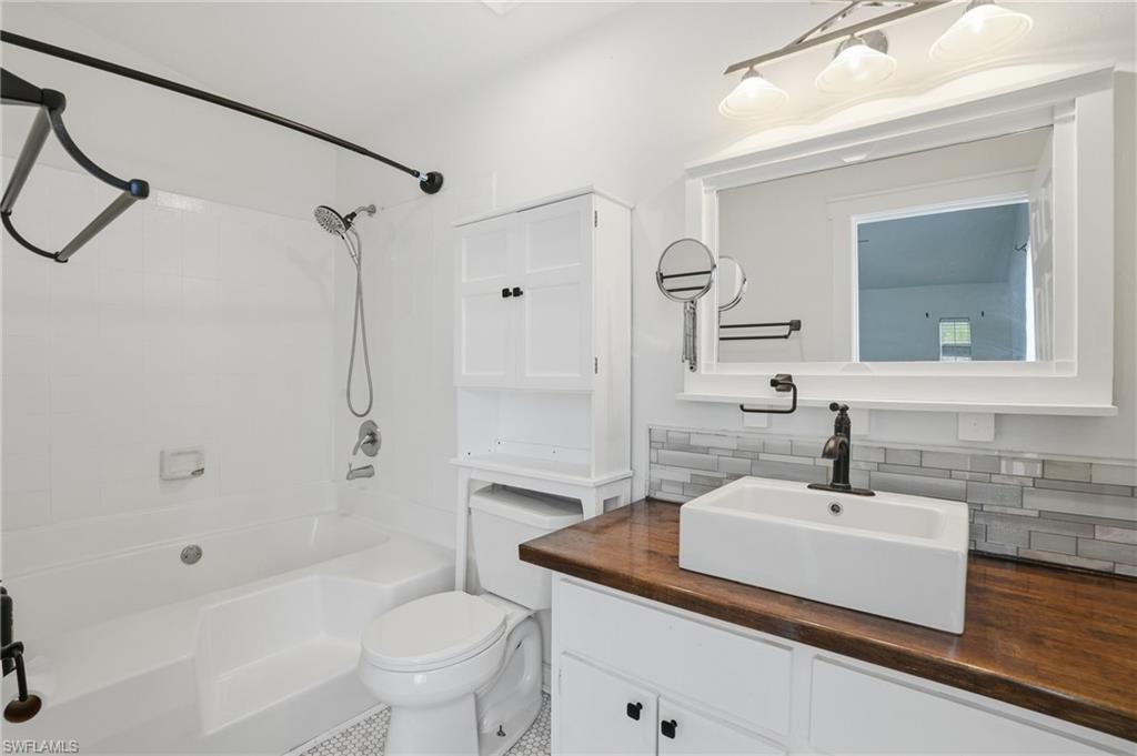 Bathroom featuring a wood-finish vanity countertop, rectangular vessel sink, white subway tile backsplash, and a white framed mirror