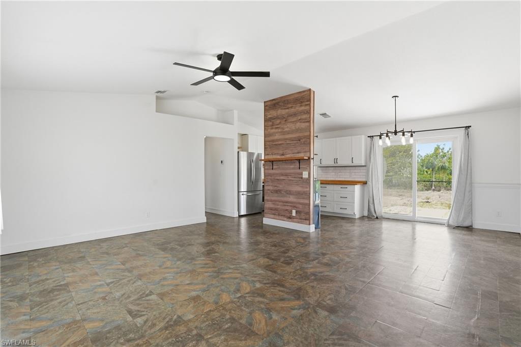 Open-concept living area featuring a modern black ceiling fan, stone-look tile flooring, and a partial wood-finish accent wall