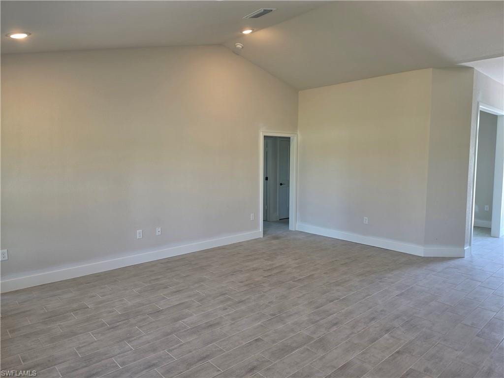 Spacious interior room featuring a vaulted ceiling with recessed lighting, light-toned walls, white baseboards, and wood-finish tile flooring
