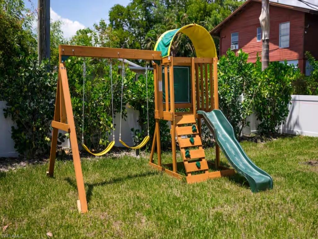 Spacious backyard featuring a wooden playset with two swings, a slide, and climbing steps