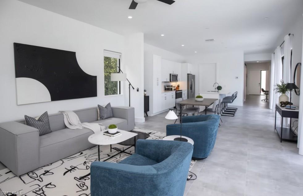Open-concept living space featuring light gray tile flooring, a contemporary ceiling fan, recessed lighting, and a kitchen with white cabinetry and stainless steel appliances