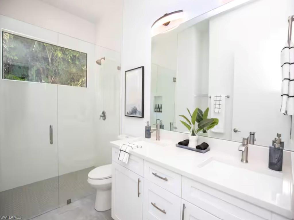 Primary bathroom featuring a dual vanity with undermount sinks and white countertops, a large mirror with integrated lighting, a walk-in shower with a glass enclosure, and a horizontal transom window