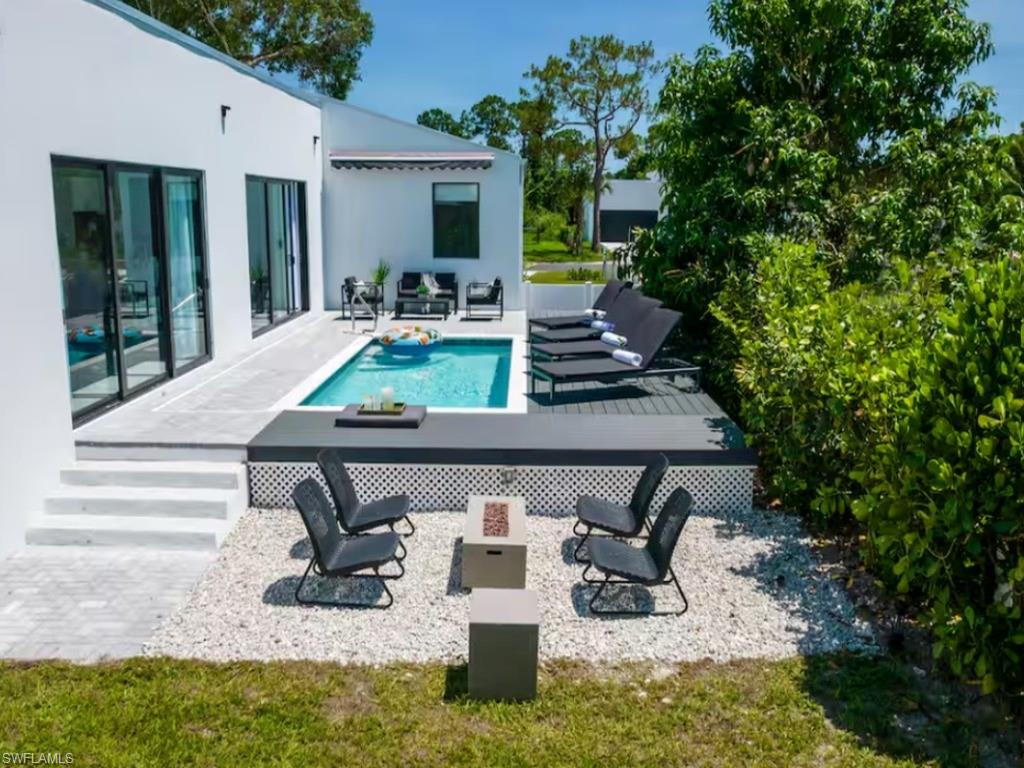 Modern exterior featuring a rectangular swimming pool, an elevated deck, sliding glass door, a white facade, and a white gravel patio with a fireplace
