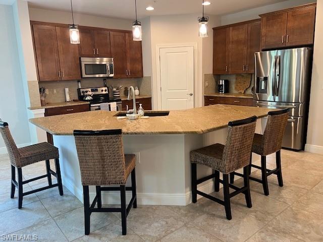 Kitchen featuring hanging light fixtures, a kitchen island with sink, backsplash, and appliances with stainless steel finishes