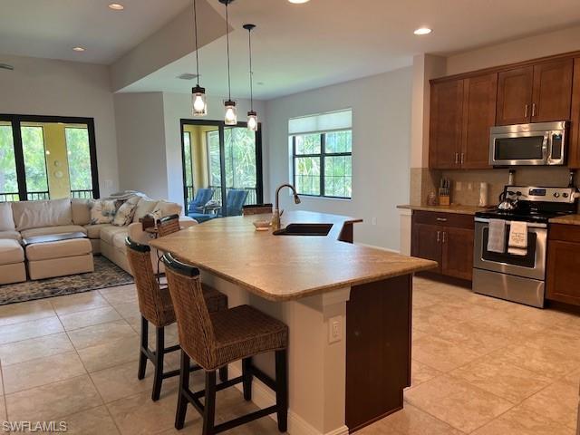 Kitchen featuring appliances with stainless steel finishes, decorative light fixtures, sink, tasteful backsplash, and light tile floors