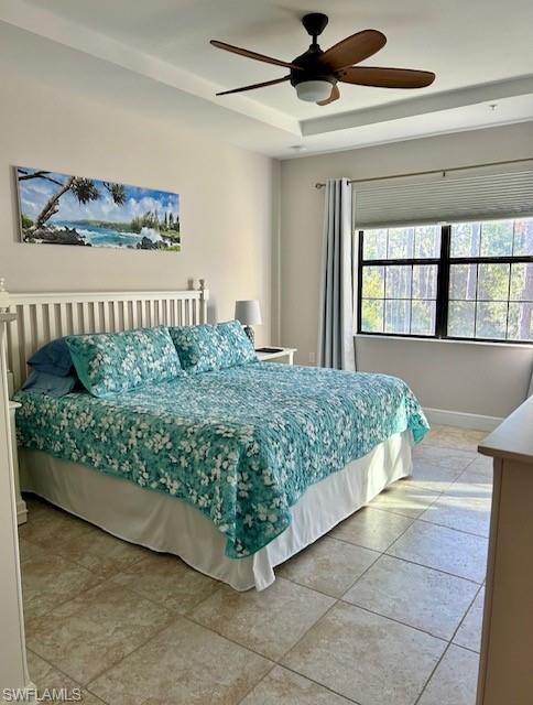 Bedroom with a raised ceiling, ceiling fan, and tile floors
