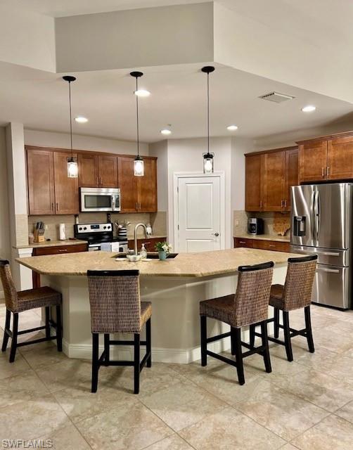 Kitchen featuring an island with sink, decorative light fixtures, a kitchen breakfast bar, and stainless steel appliances
