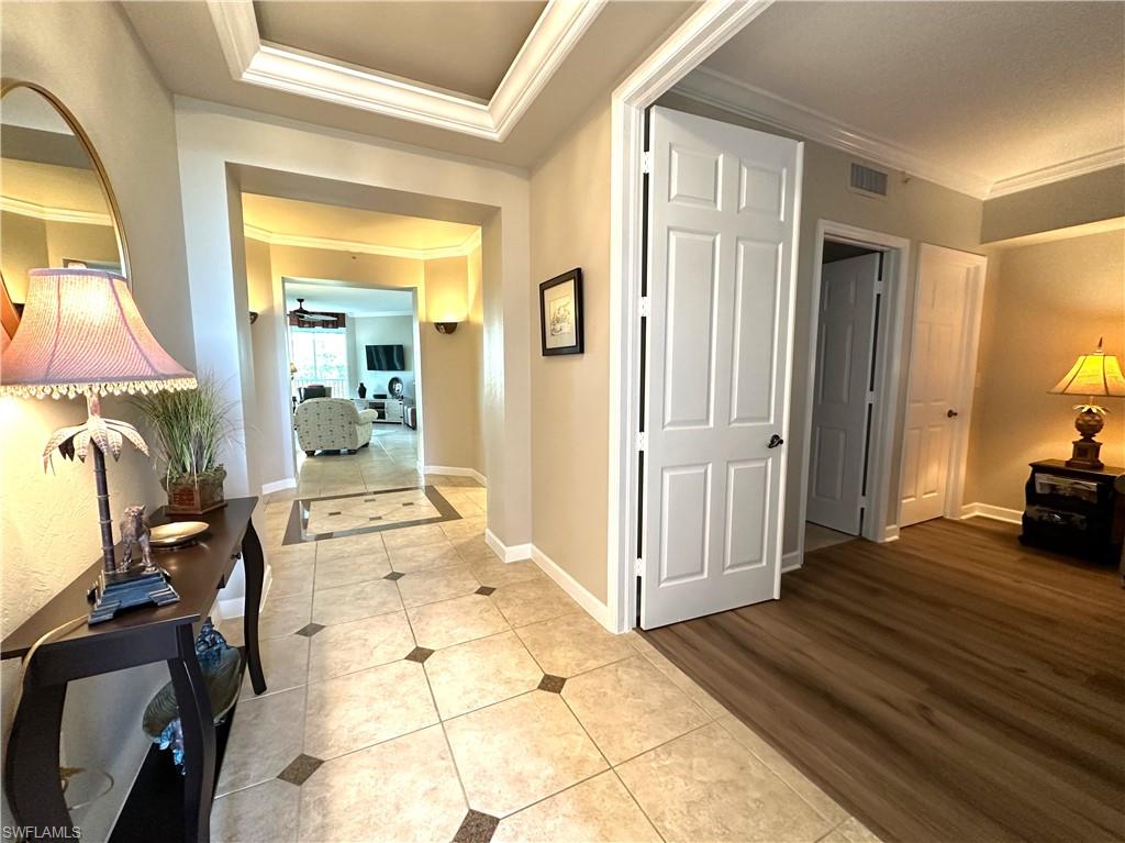 Corridor featuring wood-type flooring, a tray ceiling, and crown molding