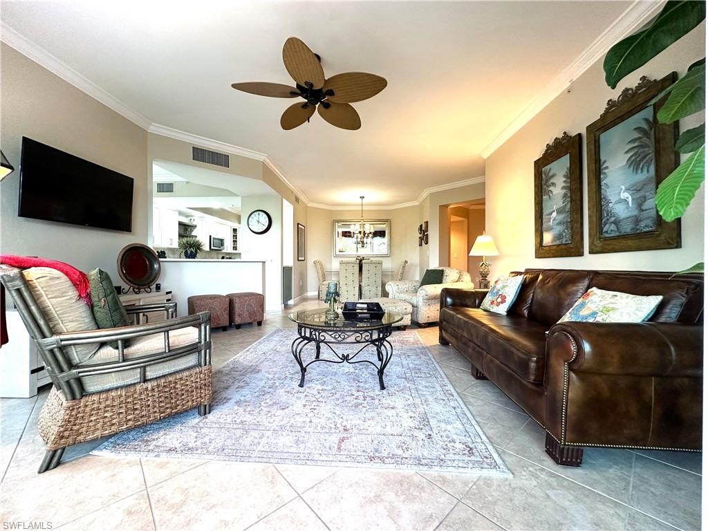 Living room with ornamental molding, tile floors, and ceiling fan with notable chandelier