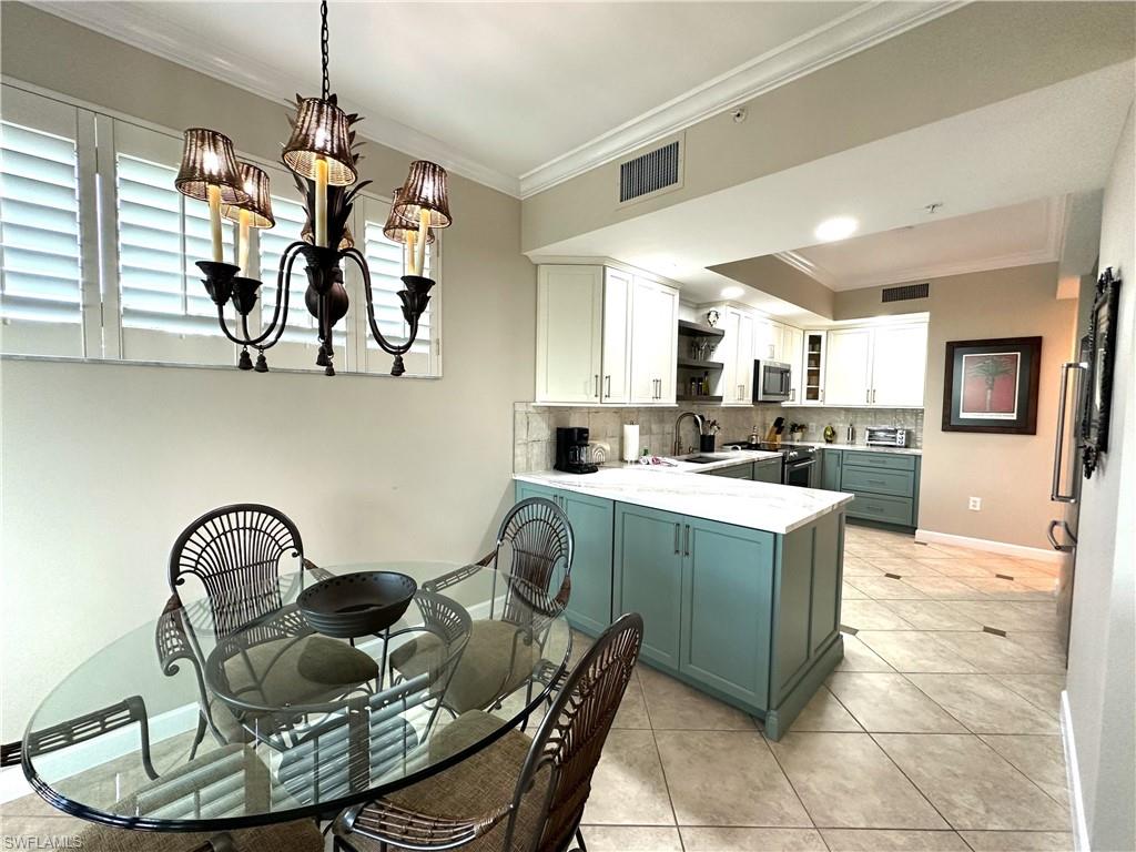 Kitchen with light tile flooring, decorative light fixtures, backsplash, white cabinets, and appliances with stainless steel finishes