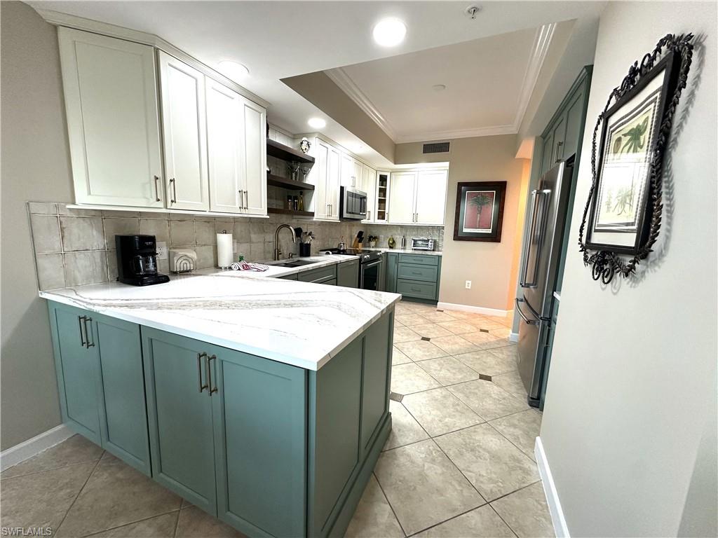 Kitchen with light stone counters, tasteful backsplash, white cabinetry, appliances with stainless steel finishes, and sink