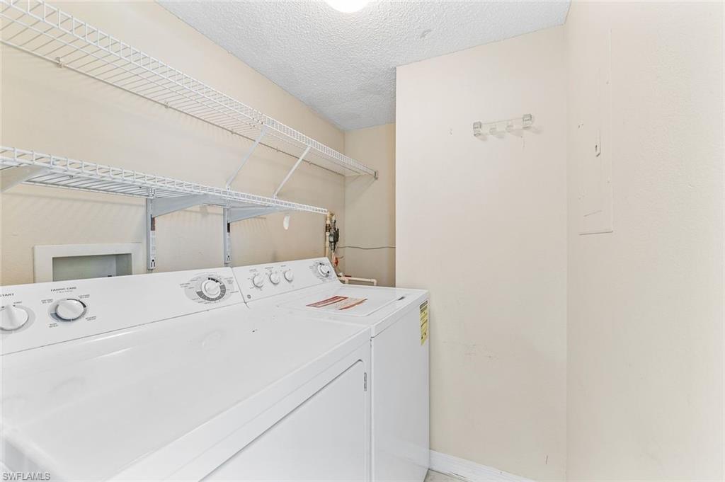 Dedicated laundry area featuring white wall shelving, a washer and dryer, water heater, and additional storage