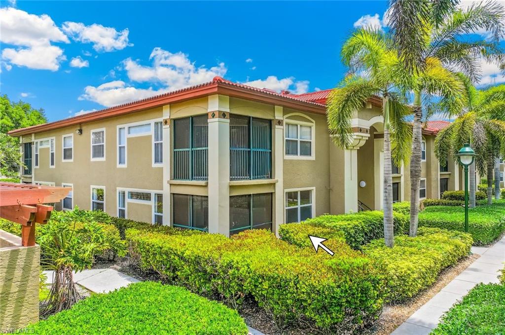 View of the rear of the ground floor unit featuring a Mediterranean-style condo building with red tile roof, stucco exterior, multiple screened balconies, mature palm trees, and manicured landscaping