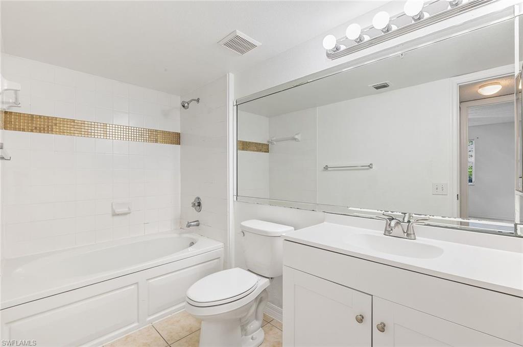 Bathroom featuring a white vanity with integrated sink, chrome faucet, and a full-width mirror, tub/shower combo, and tile flooring.