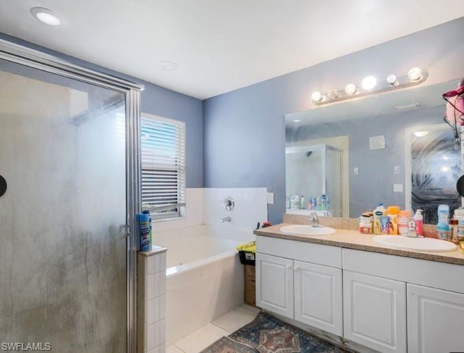 Bathroom featuring a glass-enclosed shower, built-in soaking tub, dual vanity with undermount sinks, and a framed mirror
