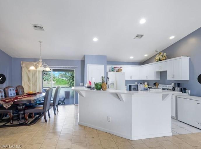 Open-concept kitchen and dining area featuring a breakfast bar, white cabinetry, tile flooring, and a sliding glass door leading to the outdoor space