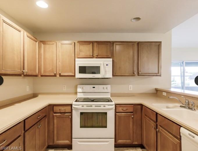 U-shaped kitchen featuring wood-finish cabinetry, solid surface countertops, white electric range, and an over-the-range microwave