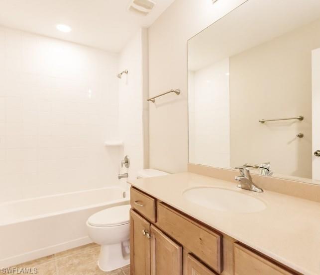 Full bathroom featuring a single vanity with wood-finish cabinetry, a large frameless mirror, a white bathtub with tile surround, and neutral floor tiling