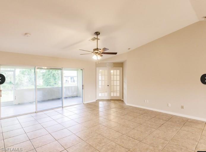 Spacious room with tile flooring, featuring a ceiling fan, sliding glass doors to a balcony, and double French doors with multiple panes