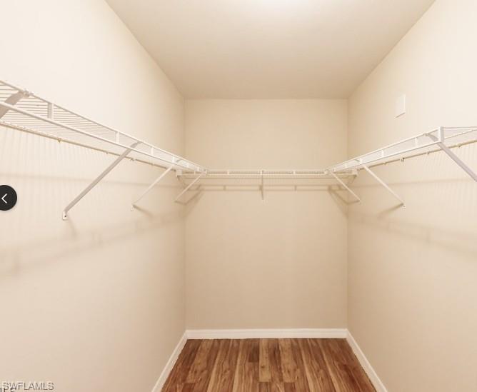 Walk-in closet featuring light beige walls, white wire shelving, white baseboards, and wood-finish flooring