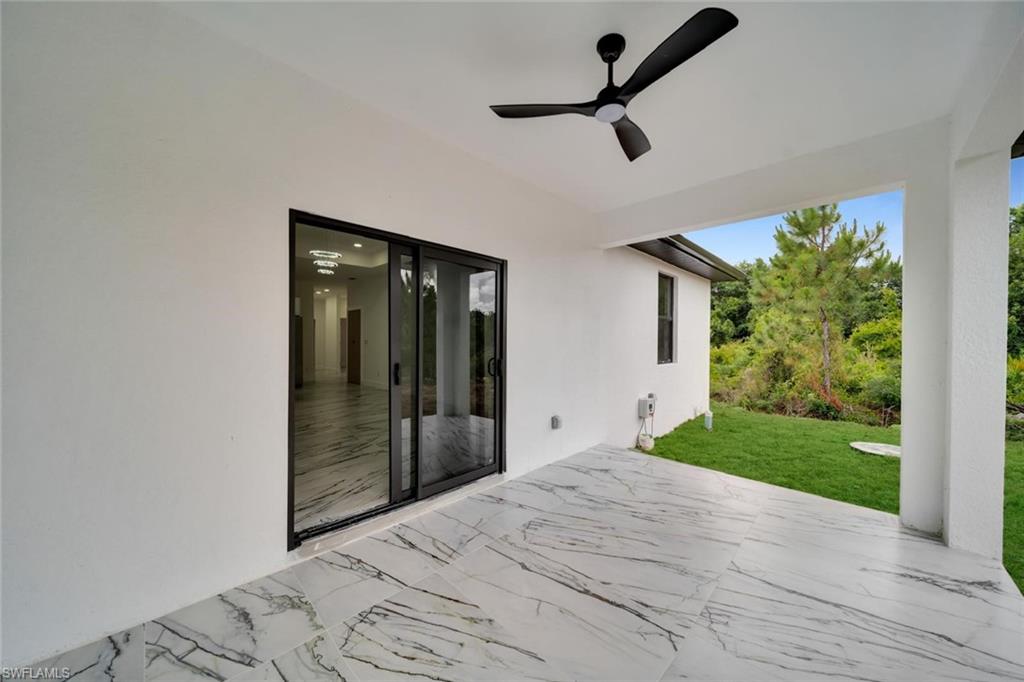Covered patio featuring large format tile flooring with distinctive veining, a ceiling fan, and black-framed sliding glass doors