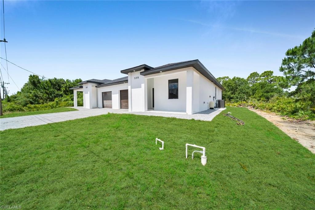 Contemporary white stucco exterior with dark trim accents, featuring a paver driveway, an attached garage, and a covered entry