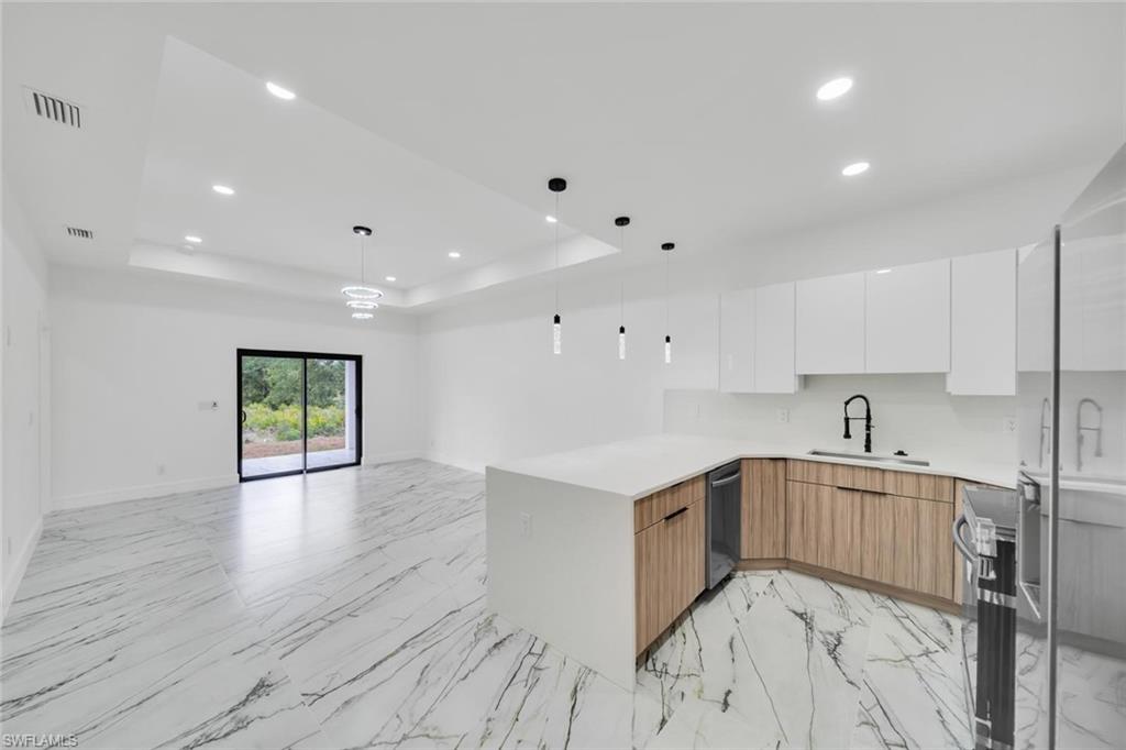 Open-concept living area featuring marble-look flooring, a kitchen island with a white countertop, two-tone cabinetry with wood-finish lower cabinets and white upper cabinets, and a sliding glass door providing outdoor access